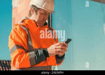 Construction engineer using mobile smart phone on site during inspection, selective focus Stock Photo