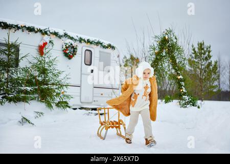 A happy little girl child in a fur coat walks in winter with a sled Stock Photo