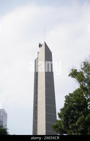 A tall minimalist tower with trees around it with a clear sky Stock Photo