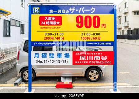 Japanese sign with prices, periods and times for parking on in Japanese with small car parked behind in parking space with the steel plate system. Stock Photo