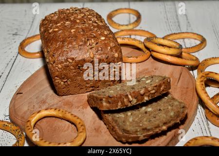 A loaf of bread made from rye flour, pieces and bagels cut from it lie on a cutting board. Stock Photo