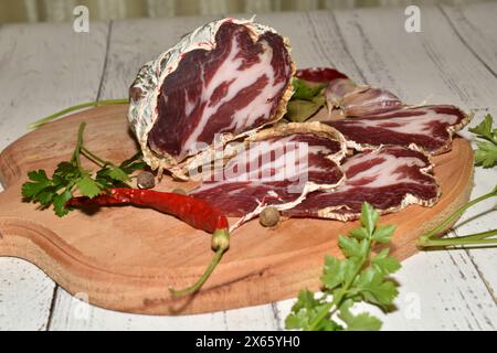 On the table on the cutting board there is a piece of smoked coppa cheese and slices cut from it. Stock Photo