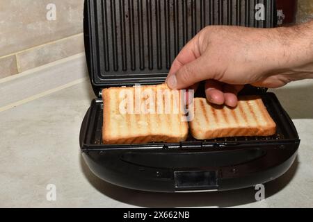 A man's hand removes ready-to-eat fried bread from a toaster. Stock Photo