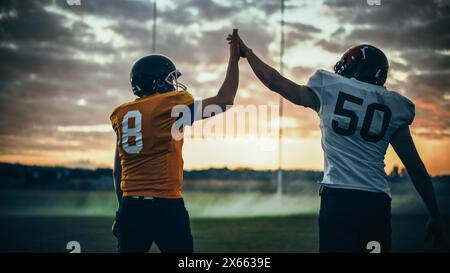 American Football Game Start Teams Ready: Two Professional Players Walk on Field Determined to Win the Match. Competitive Friends do Celebration High-Five. Back View Shot Stock Photo