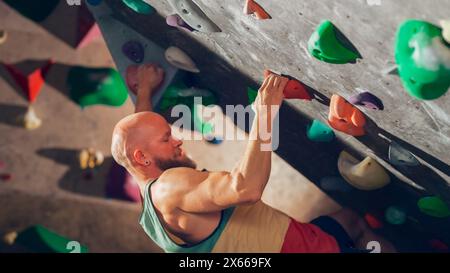 Strong Experienced Rock Climber Practicing Solo Climbing on Bouldering Wall in Gym. Man Exercising at Indoor Fitness Facility, Doing Extreme Sport for His Healthy Lifestyle Training. Close Up Portrait Stock Photo