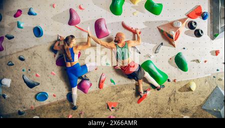 Two Experienced Rock Climbers Practicing Climbing on Bouldering Wall in a Gym. Friends Exercising at Indoor Fitness Facility, Doing Extreme Sport for Healthy Training. Giving Each Other High Five. Stock Photo