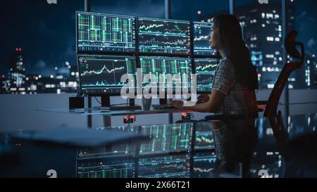 Financial Analyst Working on a Computer with Multi-Monitor Workstation with Real-Time Stocks, Commodities and Exchange Market Charts. Businesswoman Drnking Coffee at Work in Investment Bank Office. Stock Photo