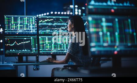 Financial Analyst Working on a Computer with Multi-Monitor Workstation with Real-Time Stocks, Commodities and Exchange Market Charts. Businesswoman at Work in Investment Broker Agency Office at Night. Stock Photo