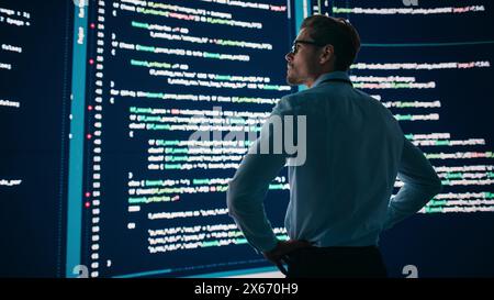 Innovative Startup Concept: Thoughtful Software Engineer Finding Solution, Planning Strategy, Standing and Doing Data Analysis on Big Wall Screen. Programmer Developing e-Commerce App. Back View Shot Stock Photo
