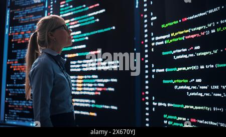 High-Tech Startup Concept: Innovative Female Software Engineer Standing and Doing Big Data Analysis on Wall Screen Showing Porgramming Code. Developing Futuristic e-Commerce App with Machine Learning Stock Photo