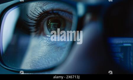 Super Close-up on Female Eye, Software Engineer Working on Computer, Programming Reflecting in Glasses. Developer Working on Innovative e-Commerce Application using Machine Learning, AI, Big Data Stock Photo