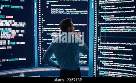 Innovative Startup Concept: Thoughtful Software Engineer Finding Solution, Solving Problem, Standing and Doing Data Analysis on Big Wall Screen. Programmer Developing e-Commerce App. Back View Shot Stock Photo