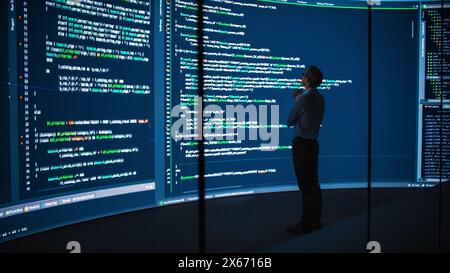 High-Tech Startup Concept: Innovative Male Software Engineer Standing, Doing Big Data Analysis on Wall Screen Showing Porgramming Code. Developing Futuristic e-Commerce App with Machine Learning. Stock Photo