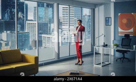 Successful Caucasian Businesswoman Using Laptop While Standing in Office Looking out of Window on Big City. Perfect Confident Female Digital Entrepreneur Developing e-Commerce Software Strategy. Stock Photo