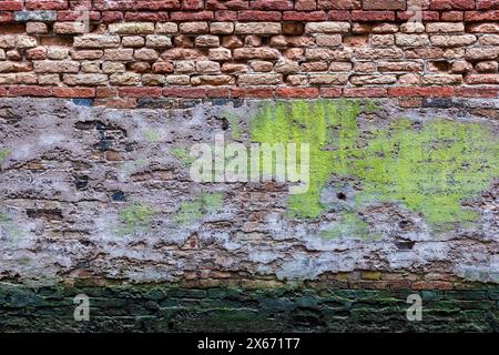 Old weathered wall vintage background of Venice canal in Italy, grunge looking brick structure texture with peeling plaster and moss. Stock Photo