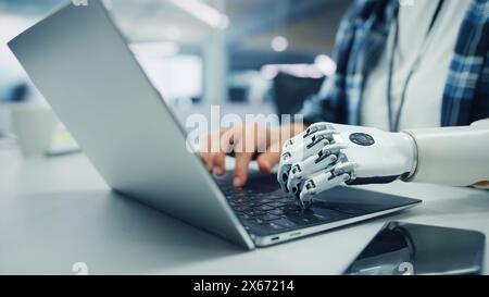 Close-up on Hands: Programmer With Disability Using Prosthetic Arm to Work on Laptop Computer. Specialist Swift and Natural Use of Myoelectric Bionic Hand To Type Code for Software Stock Photo