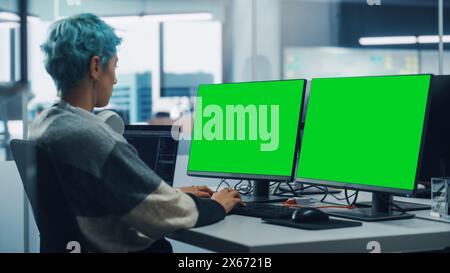 In Diverse Office: Female Programmer is Working on Green Screen Computer, Chroma key and Coding Language User Interface. Digital Entrepreneur Creating Software, e-Commerce App Design. Over Shoulder Stock Photo
