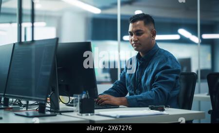 In Diverse Office: Portrait of Handsome Indian Man Working on Desktop Computer. Professional Programmer Creates Innovative Software, Modern App Design. Stylish Multi-Ethnic Authentic Workplace Stock Photo