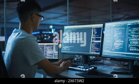 Night Office: Young Japanese Man in Working on Desktop Computer. Diverse Multi-Ethnic Team of Programmers Typing Code, Creating Modern Software, e-Commerce App Design, e-Business Programming. Stock Photo