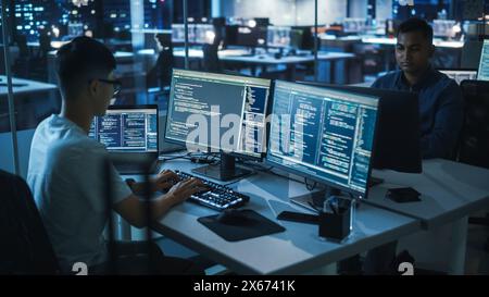 Night Office: Young Japanese Man in Working on Desktop Computer. Diverse Multi-Ethnic Team of Programmers Typing Code, Creating Modern Software, e-Commerce App Design, e-Business Programming. Stock Photo
