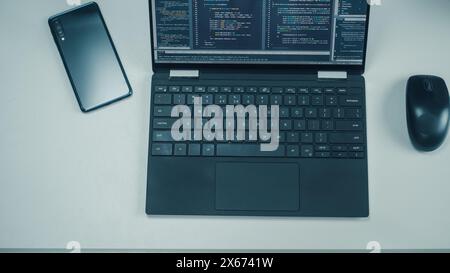 Top Down View of Laptop Computer with Developers Code on Screen, Smartphone with Rare Cameras and Computer Mouse on the Left. Professionals Software Engineers Create App on Laptop Stock Photo