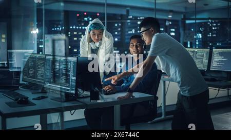 Diverse Team of Professionals Meeting in Office at Night: Brainstorming IT Programmers Use Computer Together, Talk Strategy, Discuss Planning. Software Engineers Develop Inspirational App Program Stock Photo