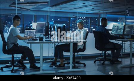 Diverse Office at Night: Multi-Ethnic Team of Young Programmers Working on Desktop Computers, Screens Show Coding Language User Interface. Software Engineers Create Innovative e-Commerce App. Stock Photo