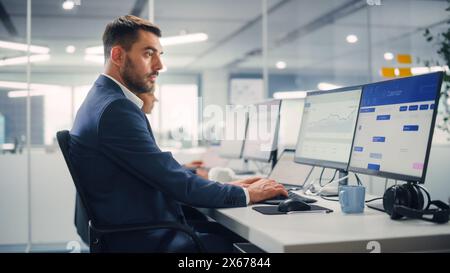 Young Businessman Using Computer in Modern Office with Colleagues. Stylish Handsome Manager Working on Desktop Computer Analyze Business Projects, Finance Data. Employees Work in Open Office. Stock Photo