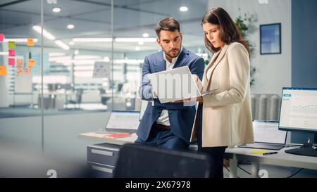 Young Manager Talking with Experienced Colleague while Using Laptop Computer in Office. Colleagues Discuss Business, Financial and Marketing Projects. Specialists Work in Diverse Team. Stock Photo
