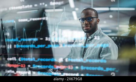 Real Office: Professional Black IT Programmer Working on Desktop Computer. Male Website Developer and Software Engineer Developing App, Video Game. Shot with Visual Effects of Running Code. Stock Photo