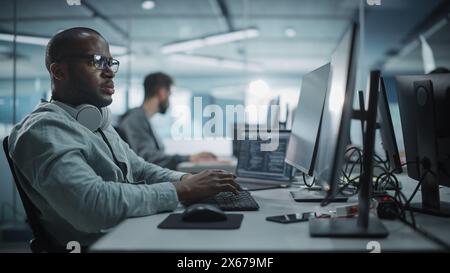Authentic Office: Enthusiastic Black IT Programmer Starts Working on Desktop Computer. Male Website Developer, Software Engineer Developing App, Video Game. Terminal with Coding Programming Language Stock Photo