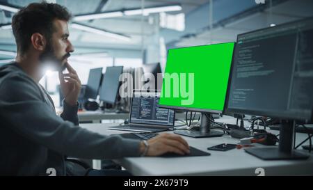 Multi-Ethnic Office: White IT Programmer Working on Computer with Green Screen Chroma Key Display. Male Software Engineer Developing App, Program, Video Game. Terminal with Code Language. Stock Photo