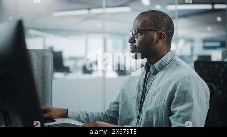 Real Office: Professional Black IT Programmer Working on Desktop Computer. Male Website Developer and Software Engineer Developing App, Video Game. Progressive, Innovative and Inspirational Person Stock Photo