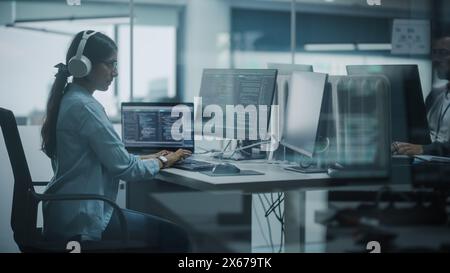 Diverse Office: Indian IT Programmer Working on Computer. Female Specialist Creating Innovative Software. Engineer Developing App, Program, Video Game. Wearing Headphones Listening Podcast, Music Stock Photo