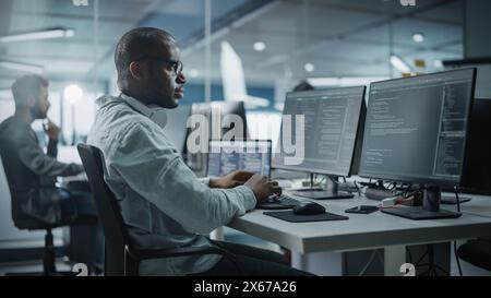 Authentic Office: Enthusiastic Black IT Programmer Starts Working on Desktop Computer. Male Website Developer, Software Engineer Developing App, Video Game. Terminal with Coding Programming Language Stock Photo