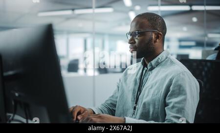 Real Office: Professional Black IT Programmer Working on Desktop Computer. Male Website Developer and Software Engineer Developing App, Video Game. Progressive, Innovative and Inspirational Person Stock Photo