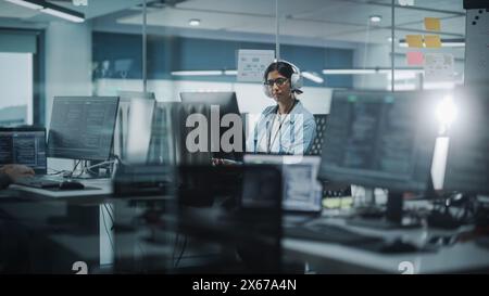 Diverse Office: Indian IT Programmer Working on Computer. Female Specialist Creating Innovative Software. Engineer Developing App, Program, Video Game. Wearing Headphones Listening Podcast, Music Stock Photo