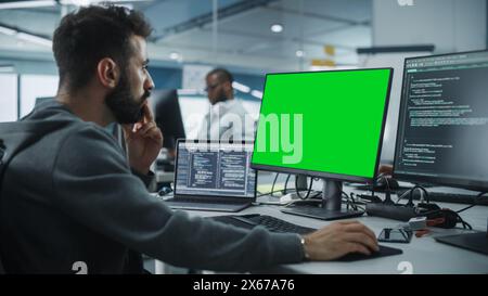Multi-Ethnic Office: White IT Programmer Working on Computer with Green Screen Chroma Key Display. Male Software Engineer Developing App, Program, Video Game. Terminal with Code Language. Stock Photo