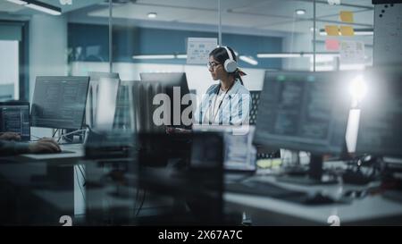 Diverse Office: Indian IT Programmer Working on Computer. Female Specialist Creating Innovative Software. Engineer Developing App, Program, Video Game. Wearing Headphones Listening Podcast, Music Stock Photo