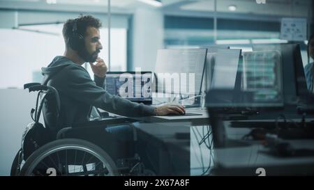 Disability-Friendly Office: Brilliant IT Programmer with Disability in a Wheelchair Working on Desktop Computer. Male Specialist Create Inspirational Software. Engineer Develop Innovative App, Program Stock Photo