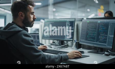 Diverse Office: IT Programmer Working on Desktop Computer. Male Specialist Creating Innovative Software Engineer Developing App, Program, Video Game. Terminal with Coding Language. Over Shoulder Stock Photo