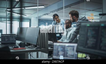 Diverse Multi-Ethnic Team Working in Modern Office: Group of IT Programmers Gather Around Desktop Computer, Talking, Finding Solution. Specialists Create Software. Engineers Develop App, Program Stock Photo