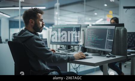 Diverse Office: IT Programmer Working on Desktop Computer. Male Specialist Creating Innovative Software Engineer Developing App, Program, Video Game. Terminal with Coding Language. Over Shoulder Stock Photo