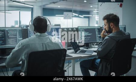 Office: Professional Black IT Programmer Uses Headphones while Working on Desktop Computer. Male Website Developer, Software Engineer Developing App, Video Game. Listening to Podcast, Music. Stock Photo