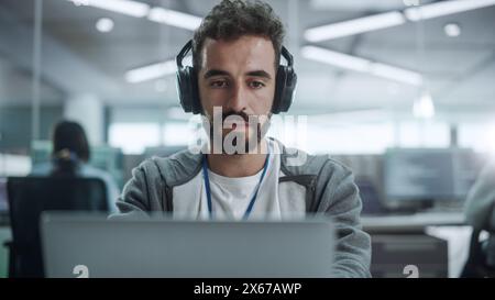 Office: Portrait of Smiling IT Programmer Wearing Headphones Working on Desktop Computer. Male Website Developer, Software Engineer Developing App, Video Game. Listening to Podcast, Music. Close-up Stock Photo