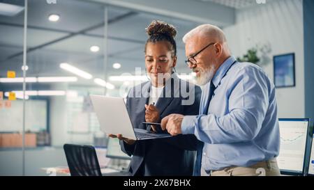 Senior Manager Talking to Experienced Confident Businessman while Using Laptop Computer in Office. Colleagues Discuss Commercial, Financial and Marketing Projects. Specialists Work in Diverse Team. Stock Photo