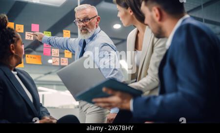 In Modern Office: Diverse Team of Managers Use Laptop and Tablet Computers at a Company Meeting Discussing Business Projects. Young, Motivated and Experienced Employees Brainstorm in Conference Room. Stock Photo