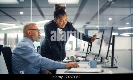 Senior Manager Talking to Experienced Confident Businessman while Using Computer in Modern Office. Colleagues Discuss Commercial, Financial and Marketing Projects. Specialists Work in Diverse Team. Stock Photo