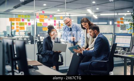In Modern Office: Diverse Team of Managers Use Laptop and Tablet Computers at a Company Meeting Discussing Business Projects. Young, Motivated and Experienced Employees Brainstorm in Conference Room. Stock Photo