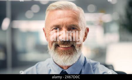 Portrait of a Confident Happy Senior Male Wearing Blue Shirt, Looking at Camera, Genuinely and Charmingly Smiling. Successful Experienced Older Man Working in Diverse Company Office. Stock Photo
